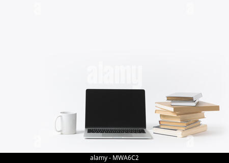 Nahaufnahme Blick auf Laptop mit leerer Bildschirm, Tasse und ein Stapel Bücher isoliert auf weißem Stockfoto