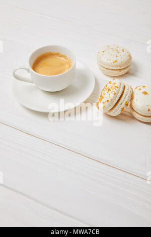 Kaffeetasse und drei Macarons auf weissem Holztisch Stockfoto