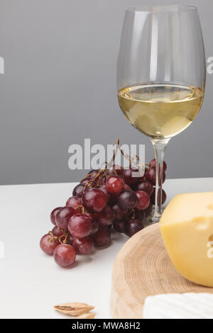 Teilweise mit Blick auf die maasdamer Käse auf Holzbrett, Glas Wein, Mandeln und Trauben auf Grau Stockfoto