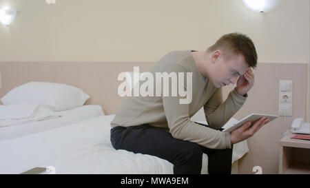 Nachdenklicher junger Mann mit Tablette im Schlafzimmer zu Hause Stockfoto