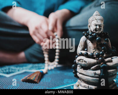 Konzentriert betende Frau mit Holz Rosenkranz mala Perlen. Namaste. Close up Statue von Buddha. Stockfoto