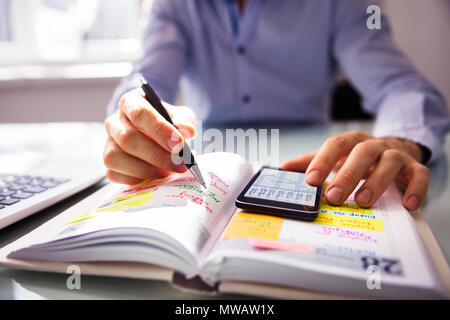 Unternehmer mit Handy beim Schreiben Zeitplan im Tagebuch Stockfoto