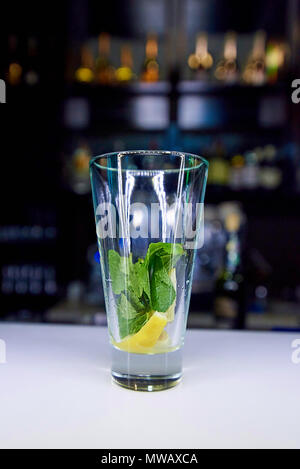 Ein leeres Glas mit einem Zweig Minze und Zitrone auf der Bar. Stockfoto