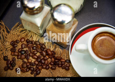 Körner von Kaffee auf einen Sack in der Nähe von eine Tasse Kaffee, Zucker und Zimt. Stockfoto