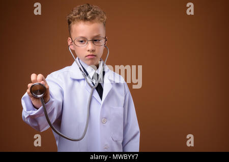 Studio shot junger Boy als Arzt gegen braunen Hintergrund Stockfoto