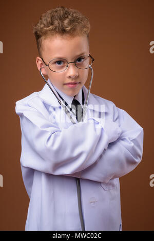 Studio shot junger Boy als Arzt gegen braunen Hintergrund Stockfoto