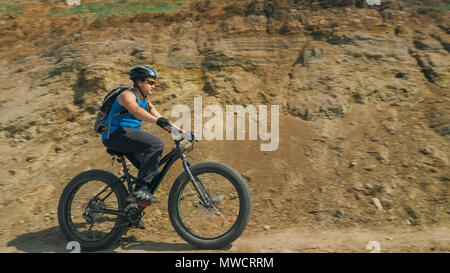 Fat bike auch fatbike oder Fat Tire Bike Im Sommer fahren auf der Straße. Der Kerl Fahrten durch die Hügel, der auf einem sand Ton weg, hinter ihm die Ufer durch. Stockfoto