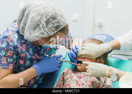 Kind mit einer Mutter ein Empfang der Zahnarzt. Das Mädchen liegt in der Stuhl, hinter ihrer Mutter. Der Arzt arbeitet mit einem Assistenten. Verfahren für drillin Stockfoto