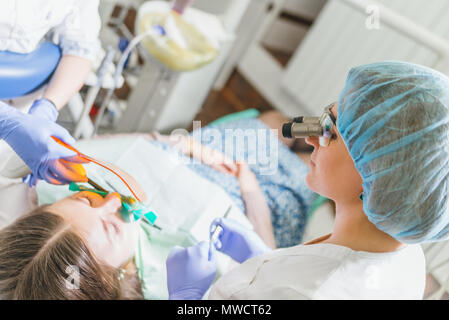 Frau beim Zahnarzt Klinik erhält der zahnmedizinischen Behandlung ein Loch in einen Zahn zu füllen. Zahnersatz und Verbundmaterial Polymerisation mit UV-Licht und Stockfoto