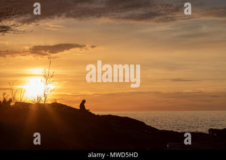 Ontonagon, Michigan - ein Mann, der liest ein Buch, wie die Sonne über den Lake Superior in Porcupine Mountains Wilderness State Park. Stockfoto