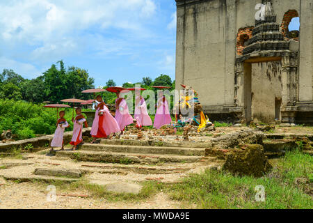 Kanchanaburi, Thailand - 24. Juli 2016: Gruppe von Mon Nonnen in rosa Roben holding Regenschirm zu Fuß aus ruiniert Buddhistischen Kirche in Kanchanaburi, Thaila Stockfoto