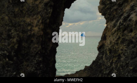 Segelboot Blick durch ein Loch im Felsen. Segelschiff Yachten mit blauen Segel im Ozean. Segelboot auf das Meer. Philippinen, Boracay. Travel Concept. Stockfoto