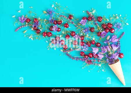 Waffel Kegel mit roten Kirschen, Kornblumen, Blue Bells und weißen Blumen blühen Blumen auf blau Oberfläche. Flach, Ansicht von oben süße Speisen floral backgro Stockfoto