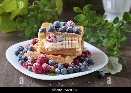 Leckere süße Waffeln mit Himbeeren und Blaubeeren auf einem alten Holztisch. Stockfoto