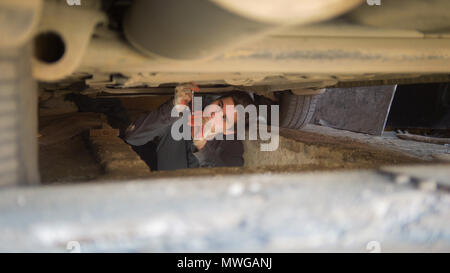 Männliche Mechaniker unter einem Auto erreichen für einen Schraubendreher in einer Garage. Stockfoto