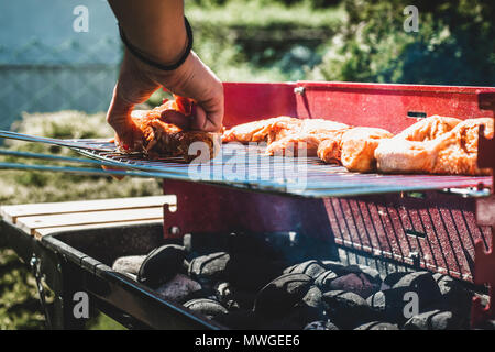 Festlegung der Hähnchen auf dem Grill. Die Frau legt Hähnchenschenkel auf dem Grill. Die Zeit gemeinsam mit der Familie am Grill. Gesellschaftliche Veranstaltungen, frien Stockfoto
