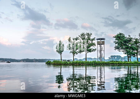 Blick auf einer kleinen Halbinsel im See Kralingse Plas in Rotterdam, die Niederlande mit ein paar Bäumen und ein Aussichtsturm, in der Dämmerung Stockfoto