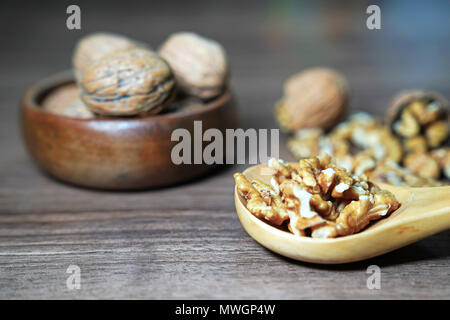 Ganze Walnüsse und kernel Walnüsse in hölzerne Schüssel und Löffel aus Holz auf dunklem Nussbaum tisch Hintergrund Stockfoto