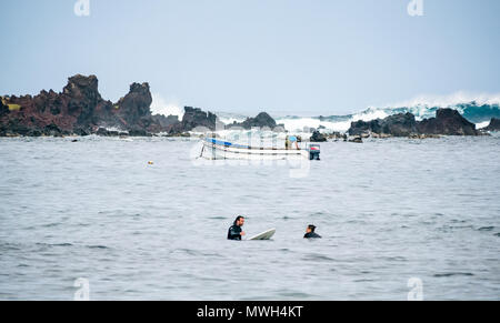 Surfer für Wave mit dive Boot und Taucher und große Welle brechen auf felsigen Küste, Hanga Roa, Rapa Nui, Chile warten Stockfoto