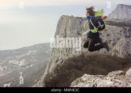 Mann mit Rucksack auf einer Klippe zu springen und schauen auf das Meer Stockfoto