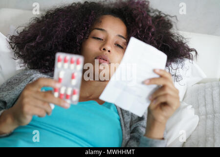 Kranke afrikanische amerikanische Mädchen mit Grippe im Bett zu Hause. Kranke junge schwarze Frau mit kaltem lesen Antibiotika Rezept für Krankheit. Stockfoto