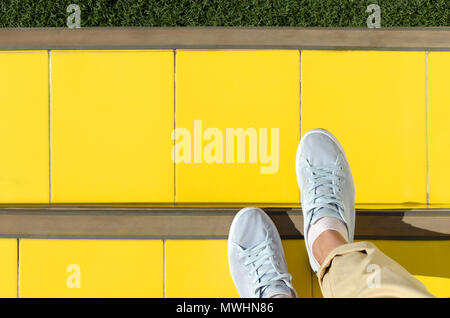Zusammenfassung Hintergrund - füß im hellblauen Sneakers sind auf Treppen mit gelben Ziegeln gedeckt, vor grünen Rasen. Leere Platz für Text. Stockfoto