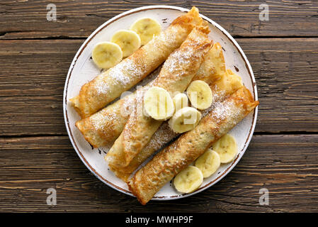 Crepes mit bananenscheiben auf Holz- Hintergrund. Ansicht von oben, flach Stockfoto