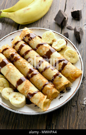 Leckere Crêpe-Rolle mit bananenscheiben auf hölzernen Tisch. Dünne Pfannkuchen, Crêpes mit Schokoladensauce. Stockfoto