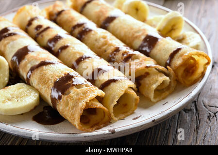 Nahaufnahme von leckeren Crêpe-Rolle mit bananenscheiben auf hölzernen Tisch. Dünne Pfannkuchen, Crêpes mit Schokoladensauce. Flache Tiefenschärfe Stockfoto