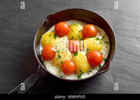 Spiegeleier mit Tomaten in der Pfanne auf schwarzen Stein Tabelle Stockfoto