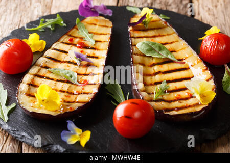 Gegrillte Auberginen und Tomaten mit Kräuter und essbare Blumen close-up auf einer Servierplatte. Horizontale Stockfoto