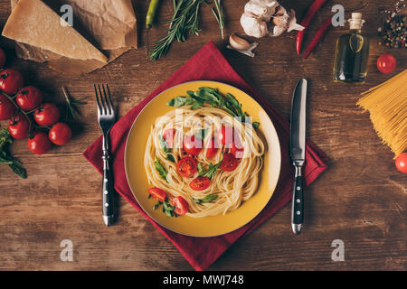 Blick von oben auf die traditionelle italienische Pasta mit Tomaten und Rucola in der Platte auf Holztisch mit Zutaten Stockfoto