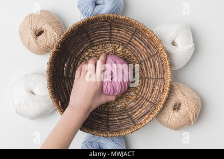 7/8-Ansicht von Frau mit rosa Garn Ball in Hand aus Weidenkorb auf weißem Hintergrund Stockfoto