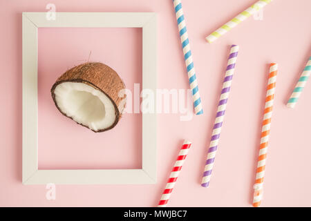 Flach von gerahmten Coconut und bunten Trinkhalmen gegen Pastell rosa Hintergrund minimal Sommer tropische Essen und Trinken kreatives Konzept. Stockfoto