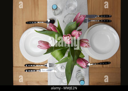 Geschirr mit Platten auf Tisch mit Blumen in der Vase Stockfoto