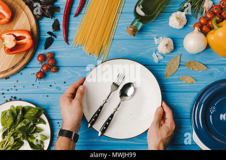 Zugeschnittenes Bild des Menschen, Teller mit Gabel und Löffel auf blauer Tisch Stockfoto