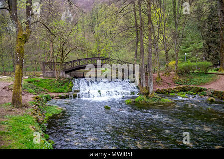 Holzbrücke mit Wasserfall im Naturpark Vrelo Bosne in der Nähe von Sarajevo, Bosnien und Herzegowina. Stockfoto