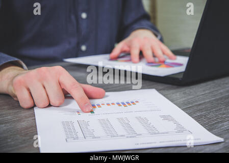 Arbeiten im Büro, am Schreibtisch, Analyse der Daten. Der Mann prüft die Daten auf die Charts, die Analyse der Kosten, Gewinne. Jahresbilanz. Der Geschäftsmann Stockfoto