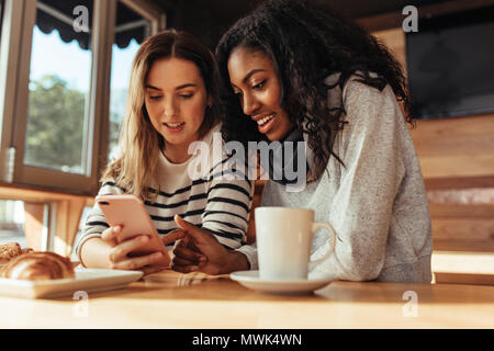 Zwei Frauen in einem Restaurant im Handy suchen. Freunde in einem Café mit Kaffee und Snacks auf den Tisch Handy suchen. Stockfoto