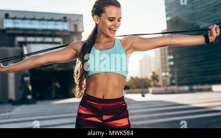 Lächelnd Sportlerin zu tun Stretching mit springseile. Frauen stehen im Freien mit Springseil und ausgestreckten Armen. Stockfoto