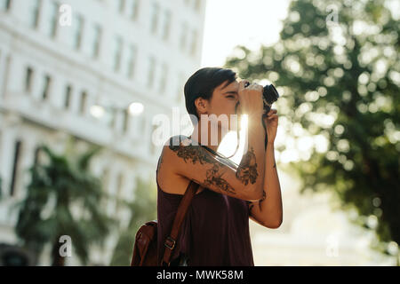 Frau Reisenden, Fotos mit Ihrer Kamera mit Sonne in den Hintergrund. Tourist mit Tattoo auf der Hand gehen in der Stadt fotografieren. Stockfoto