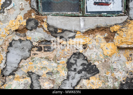 Alte rauhe rissige Mauer errichtet aus grauen Steinen mit Beton, Mörtel, Schimmel und Geschälte Farbe Flecken. Stockfoto