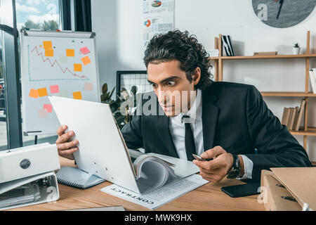 Portrait von schockiert Geschäftsmann auf Papiere, während am Arbeitsplatz sitzen Stockfoto
