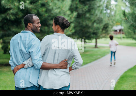 Ansicht der Rückseite des afrikanischen amerikanischen Paar umarmen und an jedem anderen Suchen in Park Stockfoto