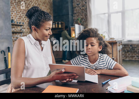 Kleines Mädchen am Küchentisch sitzen mit ihrer Mutter zeigen Sie Ihr Digital tablet Stockfoto