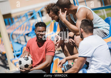 Multiethnische Gruppe Männer, die mit Fußball auf Stadion zusammen Stockfoto
