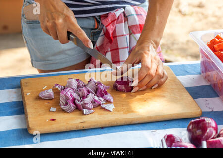 Frau Hände schneiden rote Zwiebeln auf dem hölzernen Schneidebrett. Koch hacken eine rote Zwiebel mit einem Messer für Gemüse Salat. Street Food Festival. Stockfoto