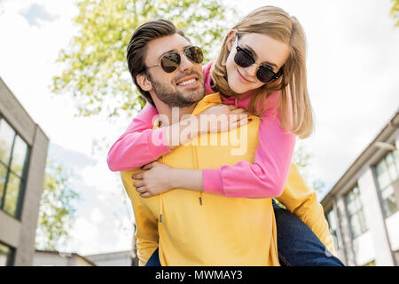 Junger Mann in Sonnenbrille tun piggyback Ride zu Freundin Stockfoto