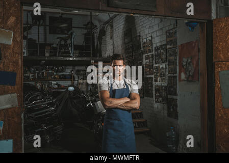 Zuversichtlich Mechaniker mit verschränkten Armen in der Werkstatt mit Anzahl Platten an der Wand Stockfoto