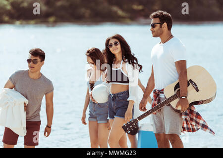 Multikulturelle junge Freunde mit Gitarre Zeit miteinander zu verbringen und Wandern am Riverside Stockfoto